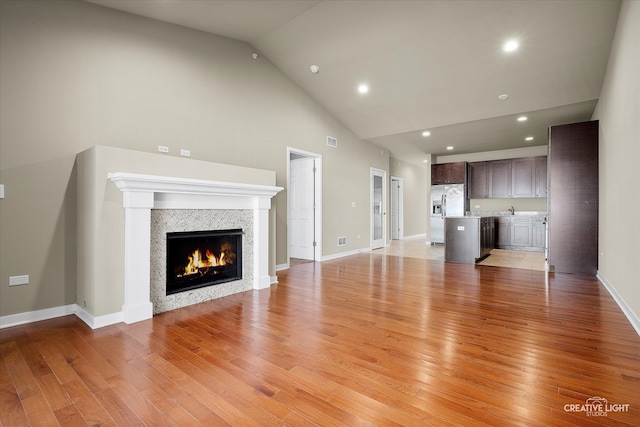 unfurnished living room with high vaulted ceiling, sink, and light hardwood / wood-style flooring