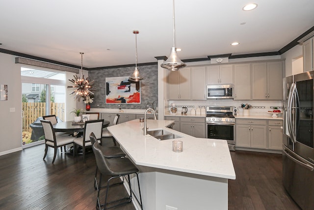 kitchen with pendant lighting, a kitchen island with sink, sink, gray cabinets, and appliances with stainless steel finishes