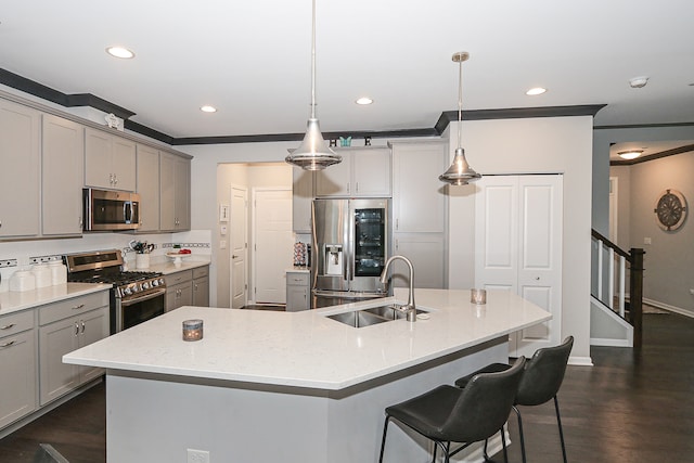 kitchen featuring a kitchen island with sink, sink, hanging light fixtures, dark hardwood / wood-style floors, and appliances with stainless steel finishes