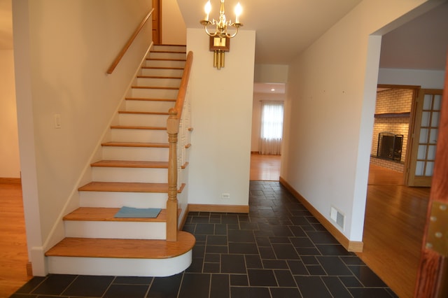 stairs with a brick fireplace, hardwood / wood-style floors, and a notable chandelier