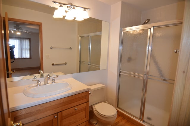 bathroom featuring a shower with door, vanity, hardwood / wood-style flooring, toilet, and ceiling fan