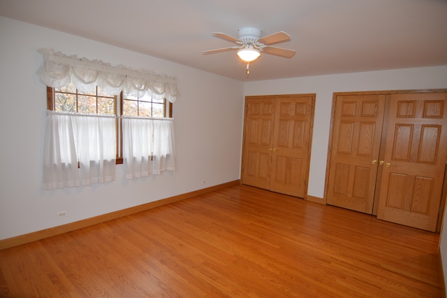 unfurnished bedroom featuring ceiling fan, wood-type flooring, and multiple closets