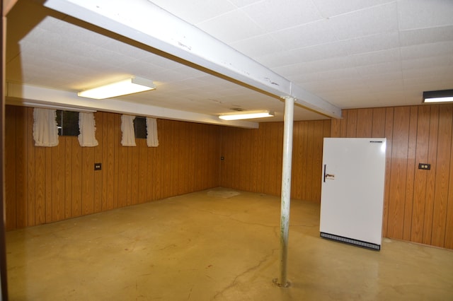 basement featuring white refrigerator and wooden walls