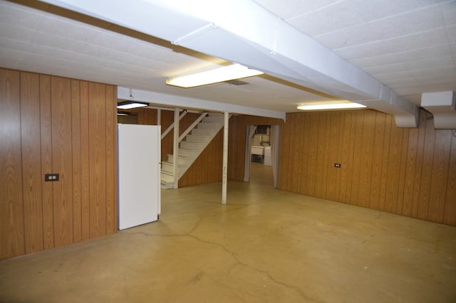 basement with wood walls and white refrigerator