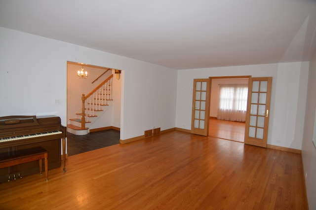 unfurnished living room featuring french doors, wood-type flooring, and a notable chandelier