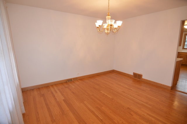 empty room with a chandelier and light hardwood / wood-style floors