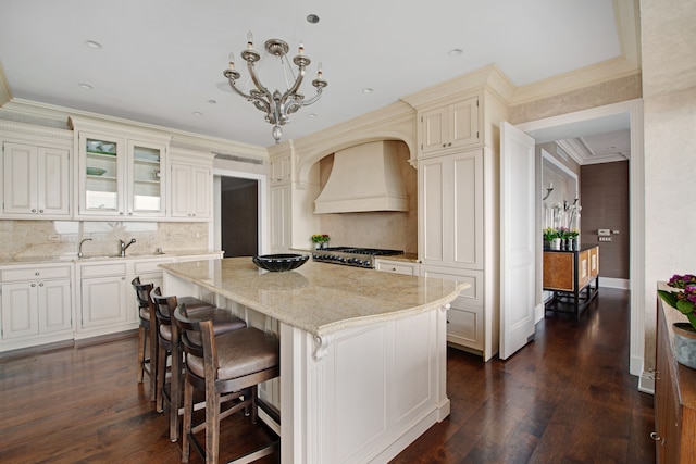 kitchen with dark hardwood / wood-style flooring, custom range hood, crown molding, a kitchen island, and decorative light fixtures