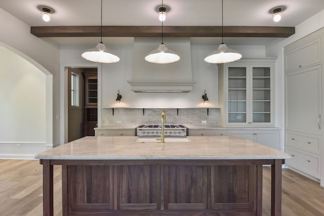 kitchen featuring beam ceiling, light hardwood / wood-style floors, light stone counters, and backsplash