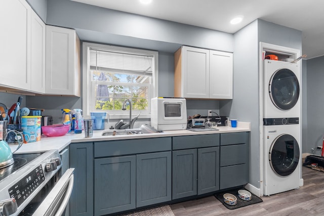 clothes washing area with hardwood / wood-style flooring, stacked washer / dryer, and sink