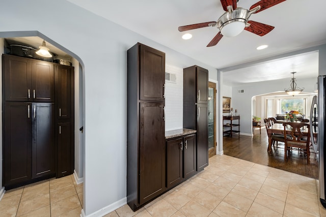 kitchen featuring light stone countertops, stainless steel fridge, dark brown cabinets, ceiling fan, and light hardwood / wood-style floors