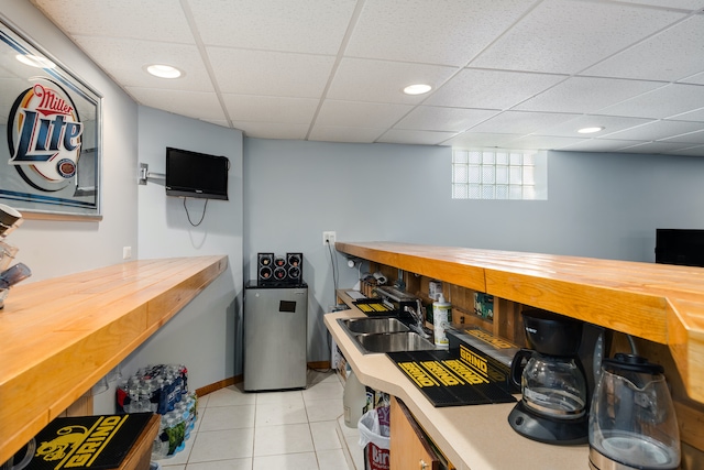 bar featuring wood counters, light tile patterned floors, a paneled ceiling, and sink