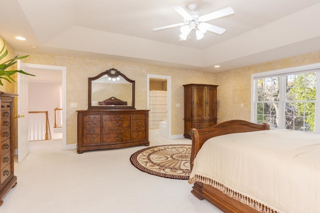 carpeted bedroom with ceiling fan, ensuite bath, and a raised ceiling