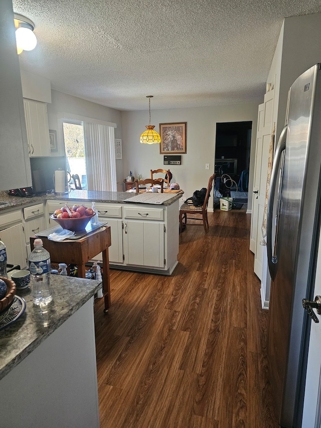 kitchen with white cabinetry, a textured ceiling, stainless steel refrigerator, dark hardwood / wood-style floors, and kitchen peninsula