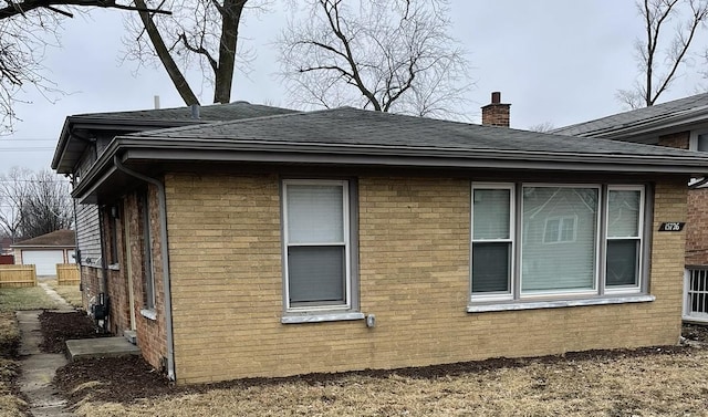 view of side of home with roof with shingles, a chimney, fence, and brick siding