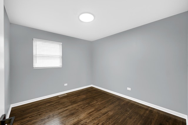 empty room with dark wood-type flooring, visible vents, and baseboards