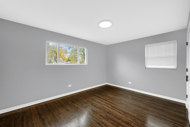 empty room featuring dark wood-style floors, baseboards, and visible vents