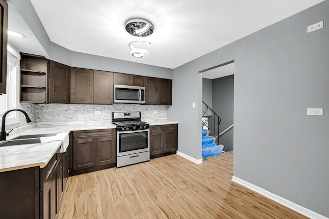 kitchen featuring light wood finished floors, appliances with stainless steel finishes, dark brown cabinets, open shelves, and a sink