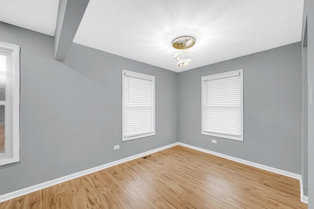 unfurnished room with light wood finished floors, baseboards, visible vents, and a notable chandelier