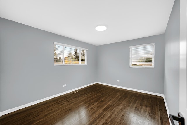 empty room with dark wood-style flooring, visible vents, and baseboards