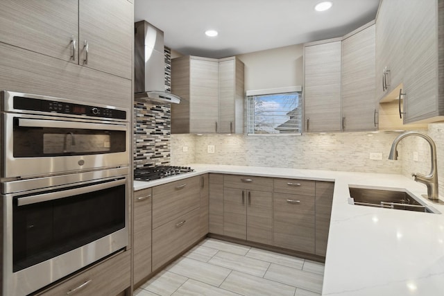 kitchen with light stone countertops, appliances with stainless steel finishes, backsplash, wall chimney exhaust hood, and sink