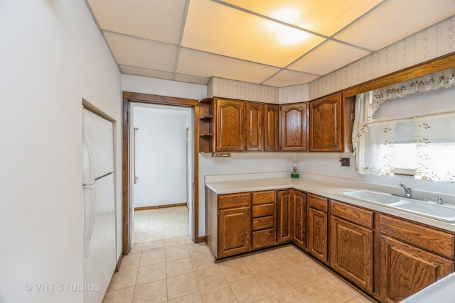 kitchen with a drop ceiling, white refrigerator, light tile patterned floors, and sink