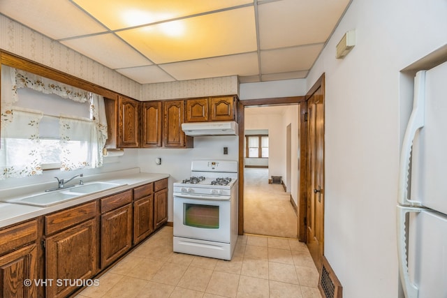 kitchen with a paneled ceiling, sink, light tile patterned floors, and white appliances