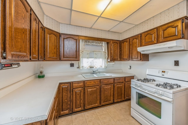 kitchen with white range with gas stovetop, light tile patterned floors, a paneled ceiling, and sink