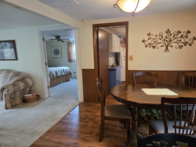 dining room featuring ceiling fan, wood walls, and dark colored carpet