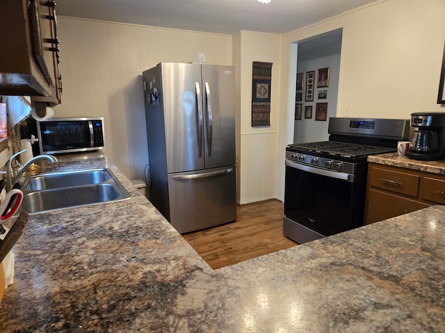 kitchen with stainless steel appliances, sink, dark brown cabinetry, and light hardwood / wood-style floors