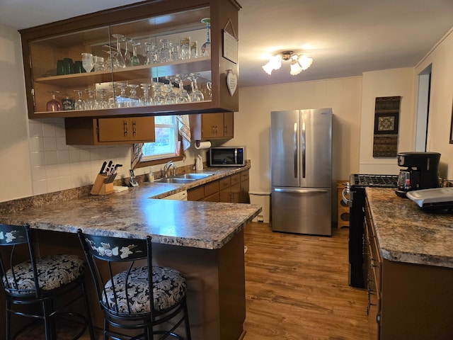 kitchen featuring sink, a breakfast bar area, stainless steel appliances, wood-type flooring, and kitchen peninsula