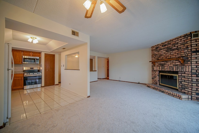 unfurnished living room featuring ceiling fan, light colored carpet, a textured ceiling, a tray ceiling, and a fireplace