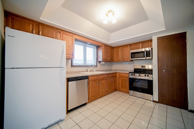 kitchen with a tray ceiling, sink, light tile patterned floors, and appliances with stainless steel finishes