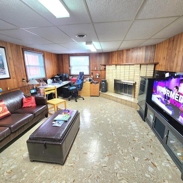 living room with a drop ceiling, wooden walls, and a fireplace