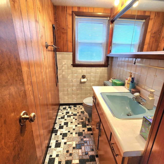 bathroom featuring a textured ceiling, vanity, wooden walls, toilet, and tile walls