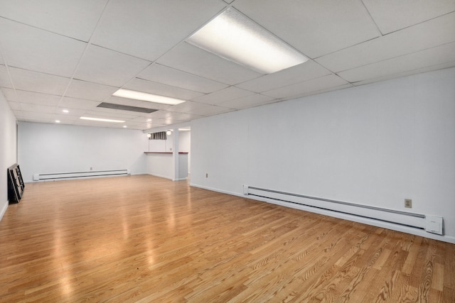 basement with baseboard heating, light wood-type flooring, and a drop ceiling