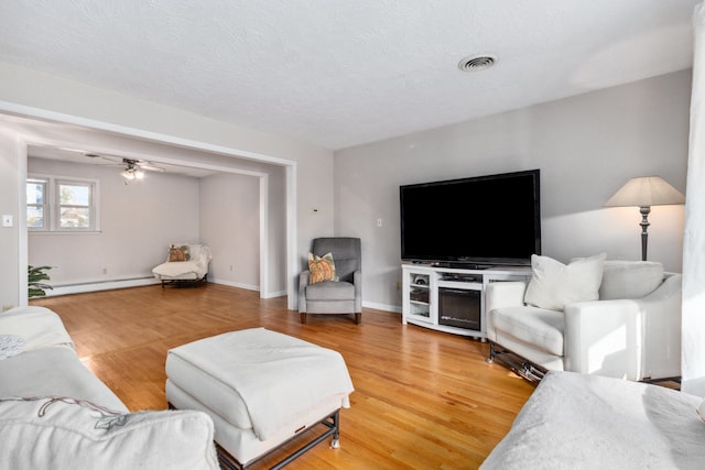 living room featuring a textured ceiling, hardwood / wood-style flooring, ceiling fan, and a baseboard heating unit