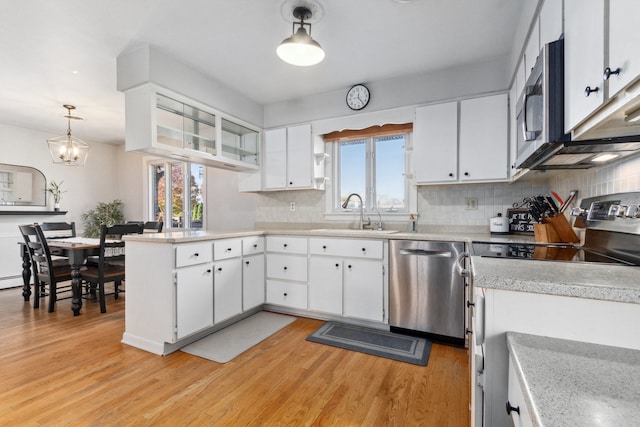 kitchen with stainless steel appliances, white cabinets, hanging light fixtures, sink, and light wood-type flooring