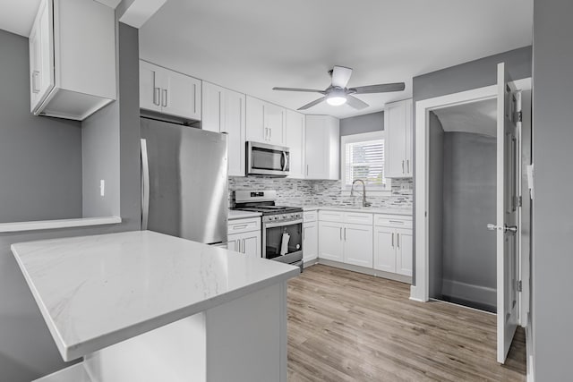 kitchen featuring kitchen peninsula, stainless steel appliances, sink, light hardwood / wood-style floors, and white cabinetry