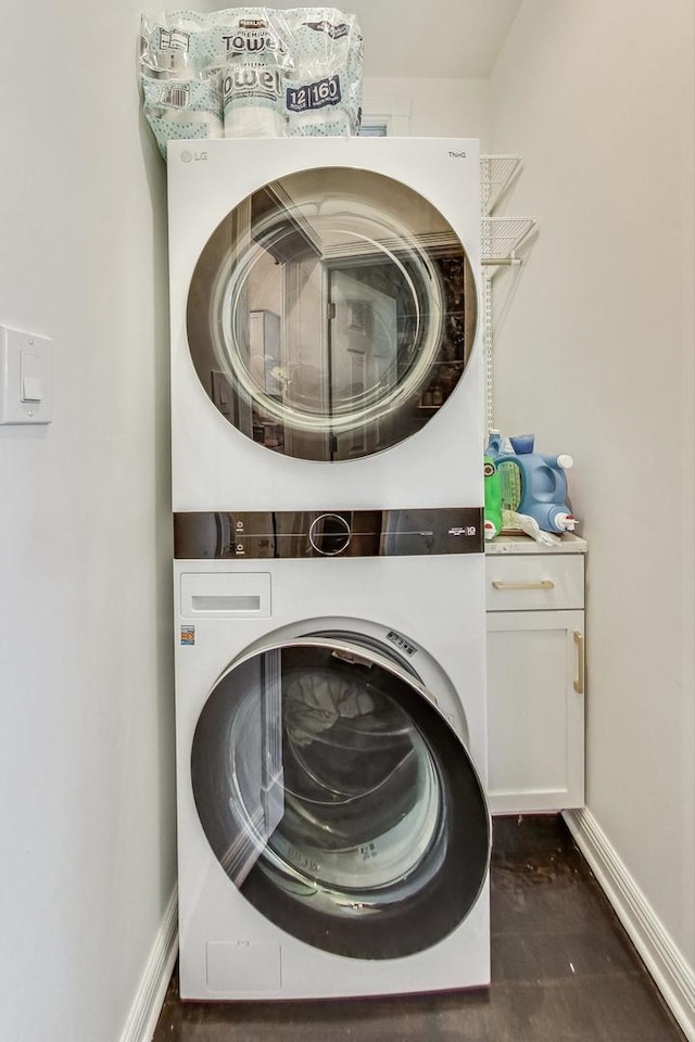 clothes washing area with stacked washing maching and dryer and cabinets