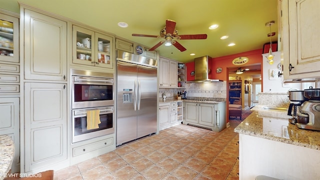 kitchen featuring decorative backsplash, wall chimney exhaust hood, ceiling fan, light tile patterned flooring, and appliances with stainless steel finishes