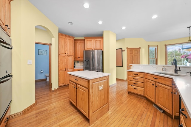 kitchen with decorative light fixtures, stainless steel fridge with ice dispenser, sink, light hardwood / wood-style floors, and a center island