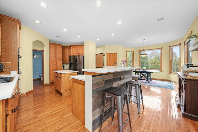 kitchen with hanging light fixtures, light hardwood / wood-style floors, a kitchen island with sink, and appliances with stainless steel finishes