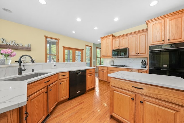 kitchen featuring light stone counters, black appliances, sink, backsplash, and light hardwood / wood-style flooring