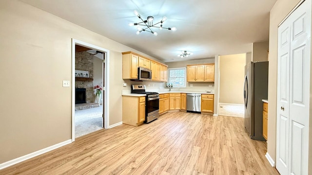 kitchen featuring light brown cabinets, a stone fireplace, light hardwood / wood-style flooring, a chandelier, and appliances with stainless steel finishes