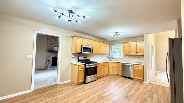 kitchen with light brown cabinets, an inviting chandelier, light hardwood / wood-style flooring, a fireplace, and stainless steel appliances