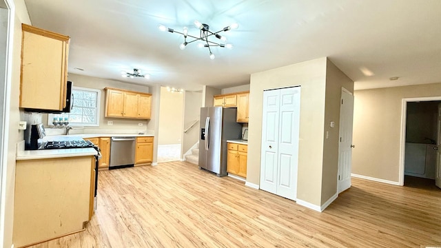 kitchen featuring light brown cabinetry, stainless steel appliances, an inviting chandelier, and light hardwood / wood-style floors