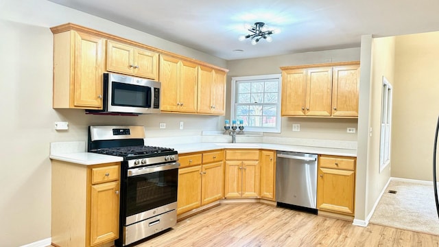 kitchen with appliances with stainless steel finishes, light brown cabinets, light hardwood / wood-style floors, and sink