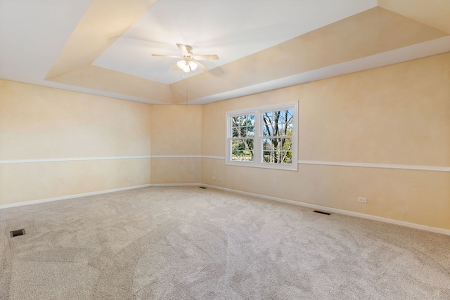 empty room with ceiling fan, a raised ceiling, and carpet floors