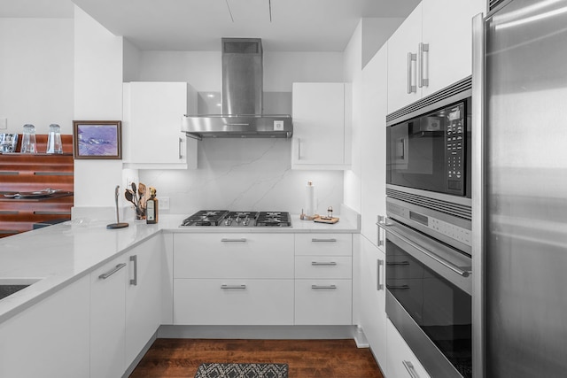 kitchen featuring white cabinets, decorative backsplash, wall chimney range hood, light stone countertops, and appliances with stainless steel finishes