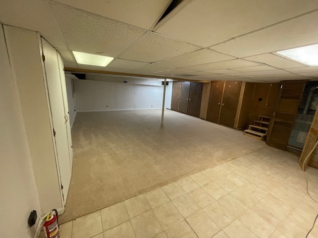 basement featuring a paneled ceiling and light colored carpet